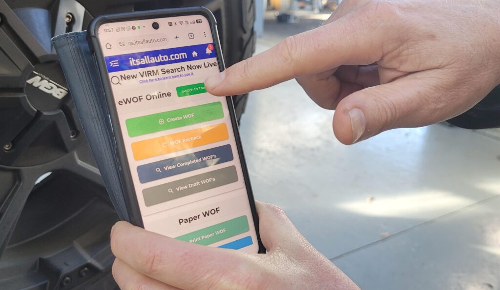 Phone displaying the itsallauto eWOF homepage with finger pointing at the button to switch to Training Mode